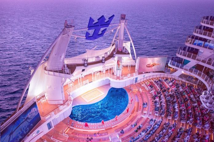 SY, Symphony of the Seas, OOH, out of home, aerial, overhead view of AquaTheater, pool, audience, performers, dancers, movie screens, sunset, evening, ocean skyline, pink, blue, and purple colors,