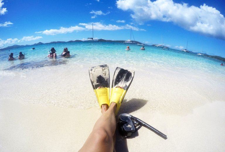 U.S. Virgin Islands, V.I., Charlotte Amalie, St. Thomas, relaxing on sandy beach, seaside, POV looking at dive flippers, snorkel by feet, snorkelers, boats, in distance, curved horizon over ocean, shore excursion,